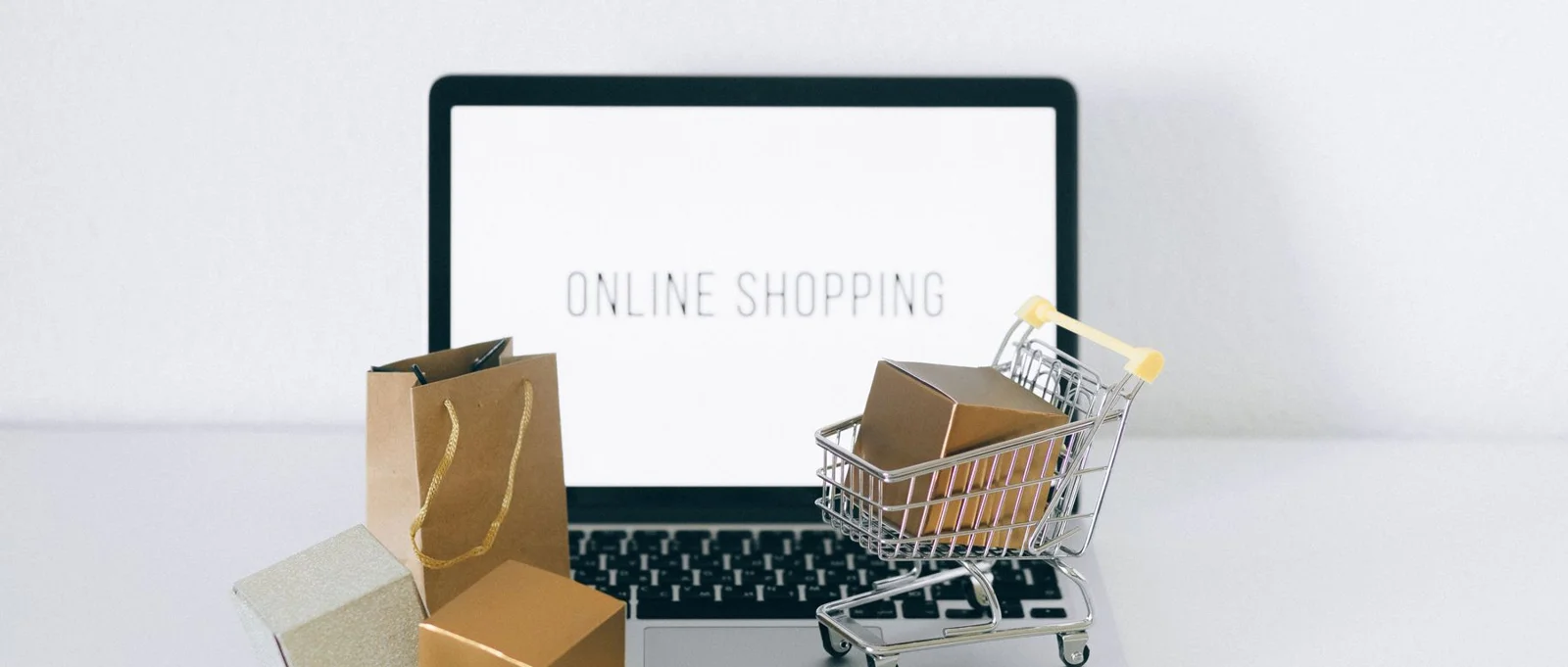 Miniature shopping cart and cardboard boxes beside a laptop